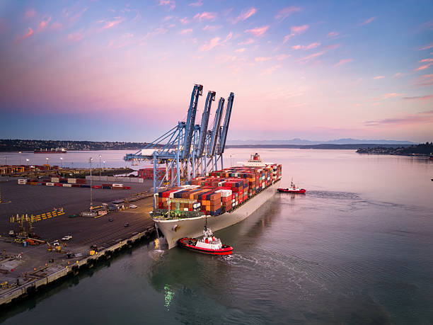 A high angle still image of a cargo ship with numerous containers on Blair Waterway, parked on container terminal in the Port of Tacoma, Washington at sunrise.