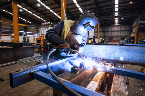 Large industrial warehouse with machinery and yellow support structures , with steel and metal processing equipment, welders welding steel bars
